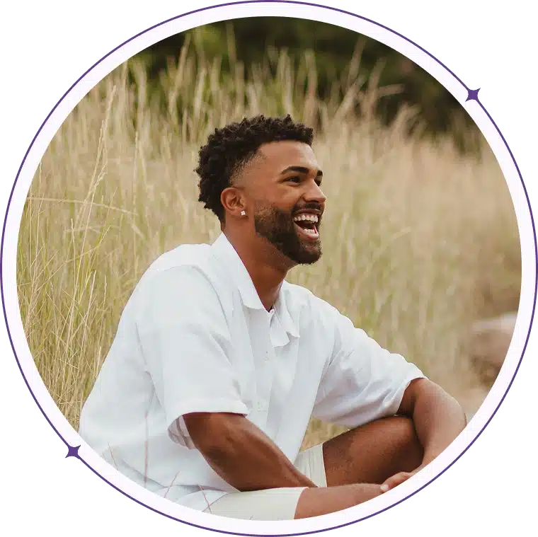 Laughing man in a grassy field, framed by a purple circle.