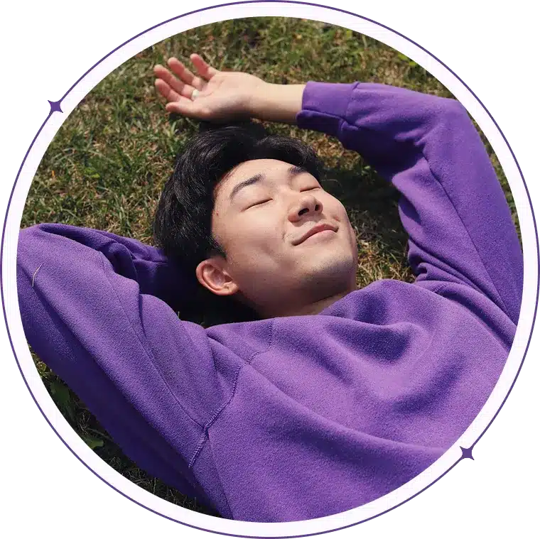 Man in purple sweatshirt resting on grass.