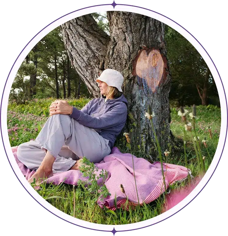 Woman in a bucket hat leaning against a tree in a clover field.