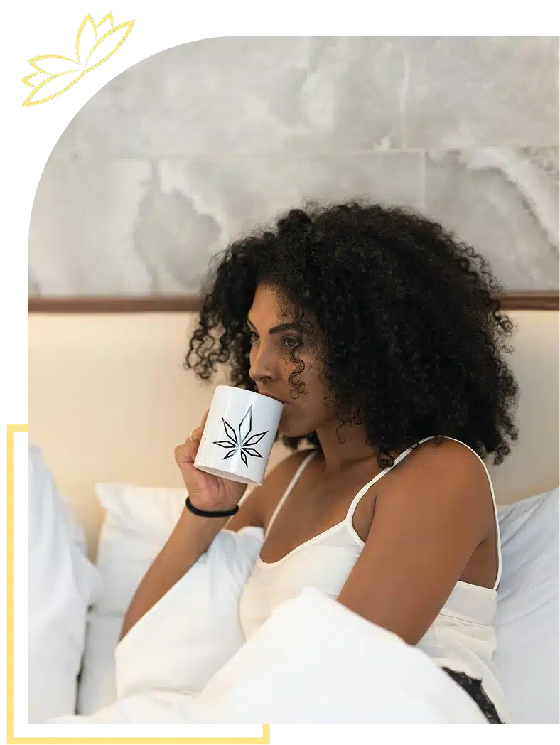 Woman with curly hair drinking from a leaf-design mug in bed.