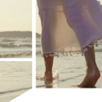 Woman in white tasseled skirt walking barefoot on a beach at sunset.