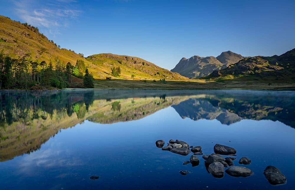 calm lake reflecting mountains and hills under blue sky