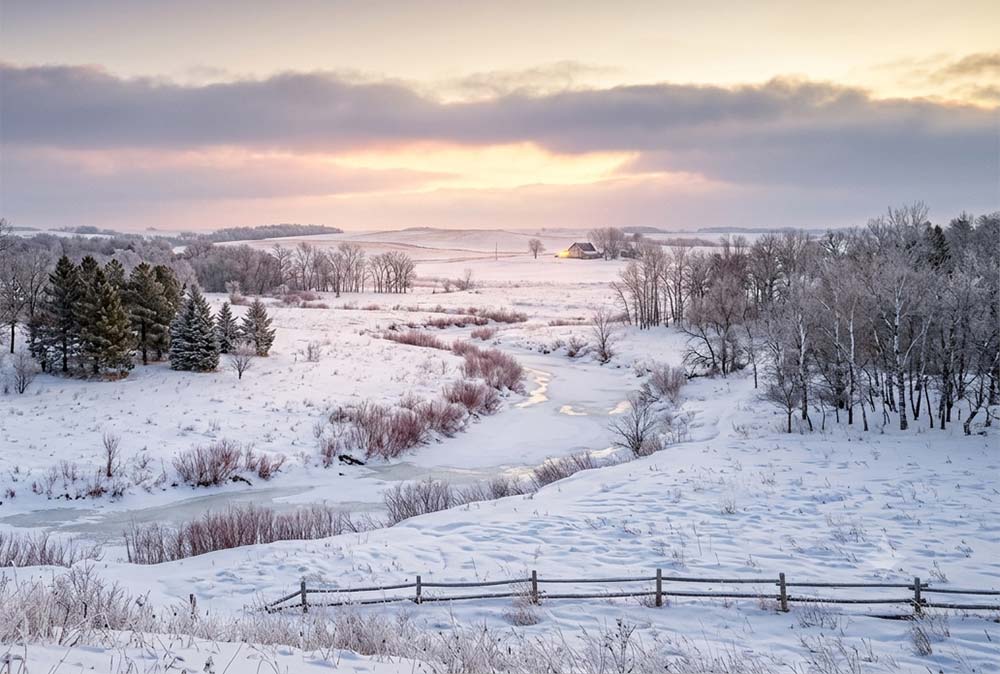 a Minnesota winter landscape at dawn or dusk with soft light breaking through clouds over a snowy scene